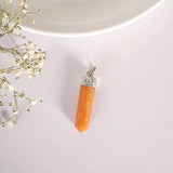 Orange crystal pendant with silver top on a light gray background with small white flowers.