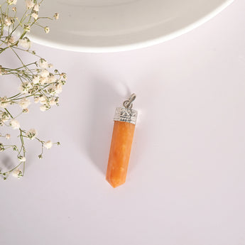 Orange crystal pendant with silver top on a light gray background with small white flowers.