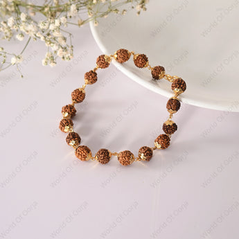 Bracelet with brown and gold beads on a white surface with flowers in the background