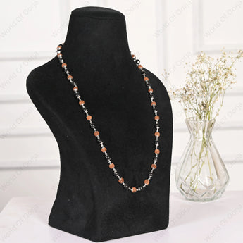 Necklace on a black mannequin bust with a vase of dried flowers in the background