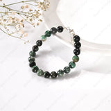 Black and green beaded bracelet on a white surface with dried flowers.