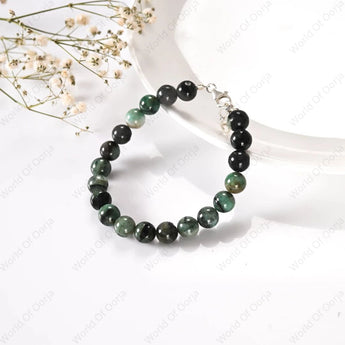 Black and green beaded bracelet on a white surface with dried flowers.