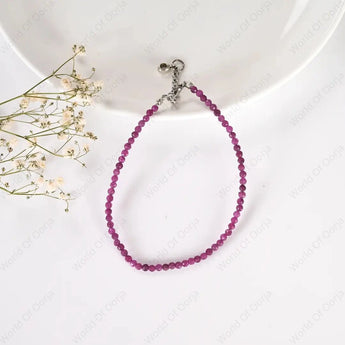 Purple beaded bracelet on a white surface with small flowers.