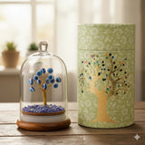 Decorative items including a tree inside a glass dome and a cylindrical container with a tree design on a wooden surface.