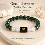 A Gemini zodiac bracelet made of Green aventurine and milky quartz beads with a central black cube bead featuring a gold Gemini zodiac symbol. The bracelet is displayed on a beige stone slab with decorative crystals and dried flowers in the background, with text overlays describing the product.