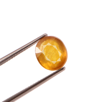 Round yellow gemstone held between tweezers on a white background