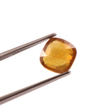 Yellow gemstone held by tweezers on a white background