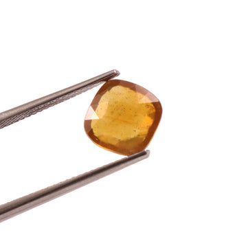 Yellow gemstone held by tweezers on a white background