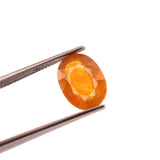 Faceted orange gemstone held by tweezers on a white background