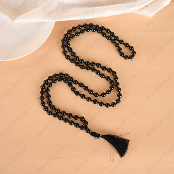 Black beaded necklace with tassel on a beige surface