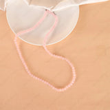 Pink beaded necklace on a beige surface with a white dish in the background