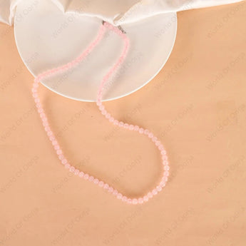Pink beaded necklace on a beige surface with a white dish in the background