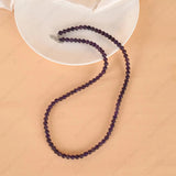 Purple beaded necklace on a beige surface with a white dish underneath