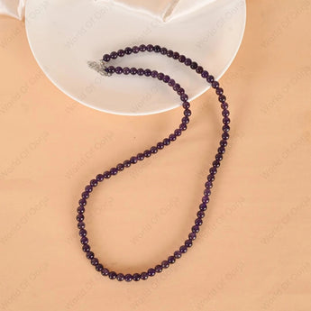 Purple beaded necklace on a beige surface with a white dish underneath