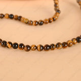 Beaded necklace with brown and black tiger eye stones on a beige background