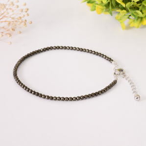 Beaded pyrite anklet on a white background with decorative elements
