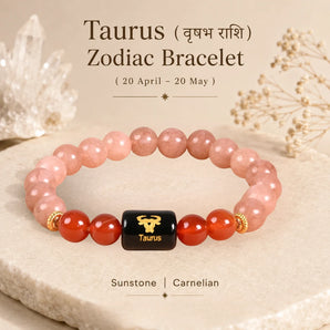 A Taurus Zodiac bracelet made of peach-pink sunstone and red carnelian beads, featuring a central black cube with a gold Taurus symbol. The bracelet is displayed on a textured stone slab with decorative crystals and dried flowers in the background, with text overlay detailing the product and its astrological significance.