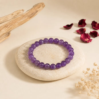 Amethyst bracelet with translucent purple crystal beads on a pale pebble with driftwood and dried rose petals – World of Oorja
