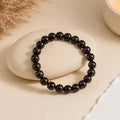 Garnet bracelet with deep wine-red glossy beads on a smooth cream stone with dried pampas and a lit candle – World of Oorja