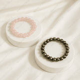 Two beaded bracelets on white stands against a soft beige background