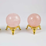 Three pink crystal balls on gold stands against a white background