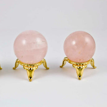 Three pink crystal balls on gold stands against a white background