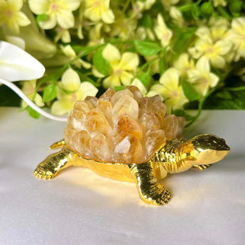 Decorative turtle figurine with a citrine on a white surface with flowers in the background
