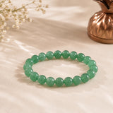 Jade bracelet with mottled green beads on soft cream fabric beside a copper kalash and white dried flowers – World of Oorja