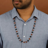 Man wearing a blue shirt with a beaded necklace featuring black, brown, and silver beads.