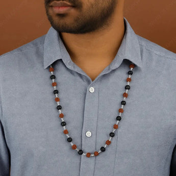 Man wearing a blue shirt with a beaded necklace featuring black, brown, and silver beads.