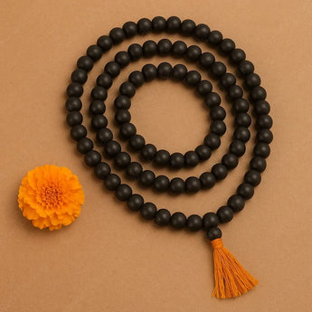 Black beaded necklace with orange tassel and flower on a brown background