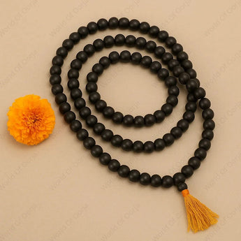 Black beaded necklace with a yellow tassel and flower on a beige background
