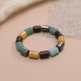 A beaded stretch bracelet featuring rectangular stone beads in green aventurine, pyrite, tiger eye, citrine displayed on a soft beige surface.
