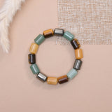 A beaded stretch bracelet made of cylindrical stone beads of green aventurine, pyrite, tiger eye, citrine  arranged in a circle on a beige background with decorative fabric and faux fur props.
