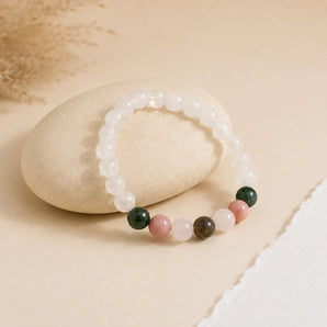 Pregnancy bracelet with milky moonstone beads and green, pink and peach accents draped over a beige pebble – World of Oorja