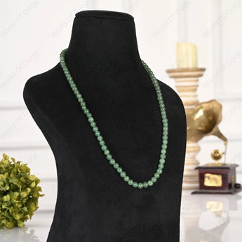 Green beaded necklace on a black mannequin bust with a blurred decorative background