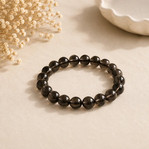 Smoky Quartz bracelet with translucent smoky brown beads on a warm beige surface with dried baby breath – World of Oorja