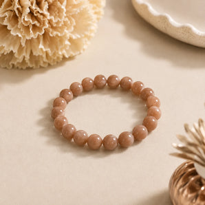 Sunstone bracelet with warm peachy caramel beads on a beige surface with a dried carnation and copper vessel – World of Oorja