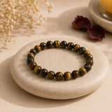 Tiger Eye bracelet with golden-brown banded beads and chatoyant shimmer resting on a flat cream pebble – World of Oorja