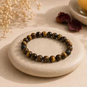 Tiger Eye bracelet with golden-brown banded beads and chatoyant shimmer resting on a flat cream pebble – World of Oorja